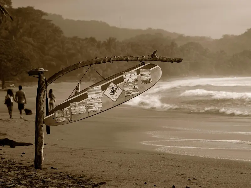 Wandelaars op het strand van Sámara met een surfplank als wegwijzer aan een drijfhouten paal