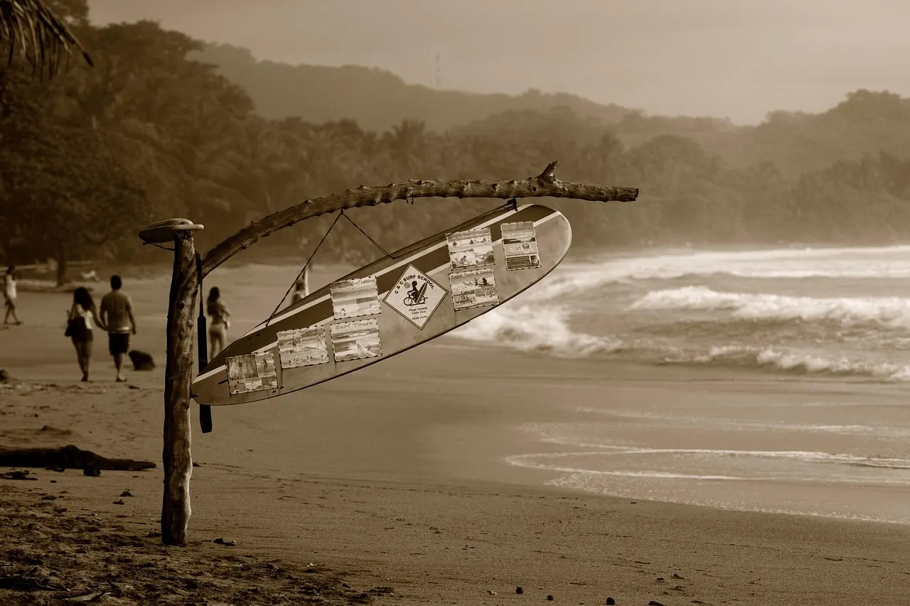 Wandelaars op het strand van Sámara met een surfplank als wegwijzer aan een drijfhouten paal