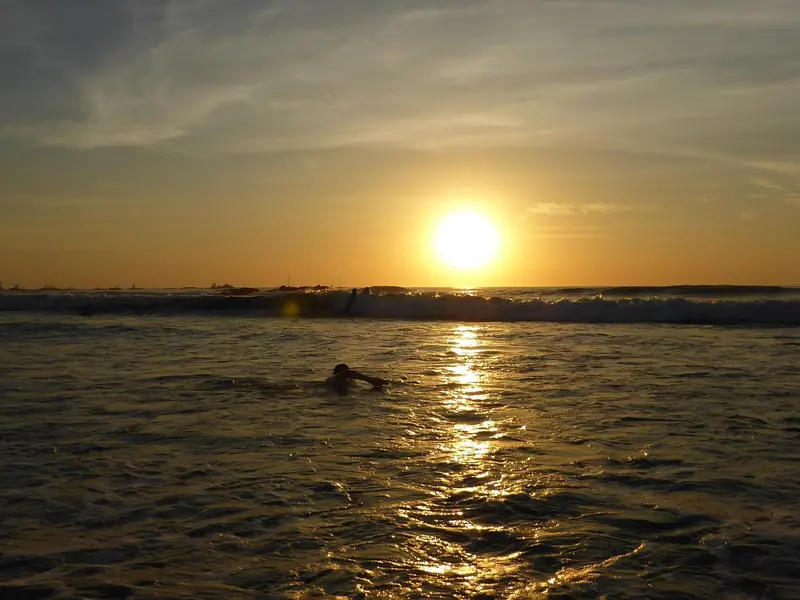 Zwemmer in zee bij zonsondergang boven de Stille Oceaan in de baai van Tamarindo